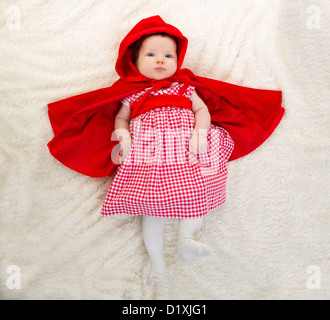 Baby Little Red Riding Hood on white fur lying with open cape Stock Photo