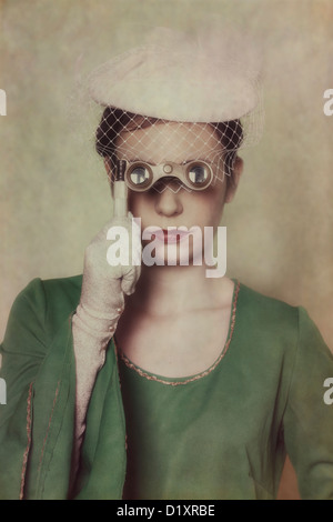 a woman in a green dress with hat is looking through a lorgnette Stock Photo