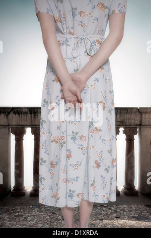 a woman in a vintage floral dress is standing on a balcony Stock Photo