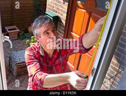 DOUBLE GLAZING Man working at open front window of domestic home for security repair safety maintenance work Stock Photo