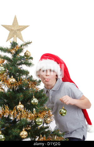 Boy with santa hat sticking out tongue at the Christmas tree on white background Stock Photo