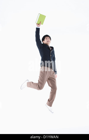 a male student wearing school uniform jumping while holding a book Stock Photo