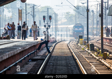 Young man crossing tracks in front of an arriving train, New Delhi Raliway Station, New Delhi, India Stock Photo