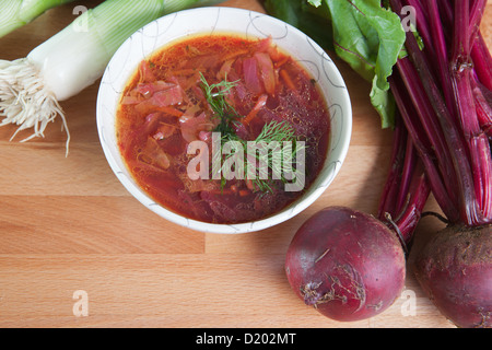 A single serving of vegetarian borscht stew on a wooden table garnished with fresh whole beets and green onions. Stock Photo
