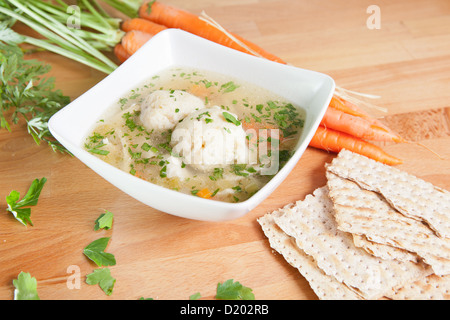 A single serving of kosher Matzah ball soup on a wooden table garnished with fresh carrots and Matzo crackers Stock Photo
