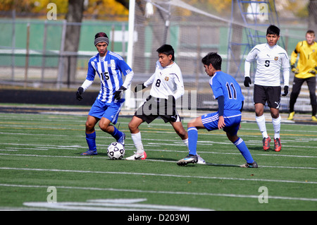 Soccer Defender works deep in his end of the pitch to clear the ball away opposing forwards during a high school match. Stock Photo