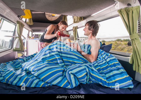 Women squeezing ketchup onto burger while serving breakfast in bed inside a camper van. Stock Photo
