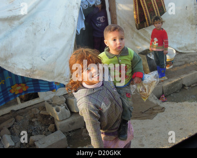 The big sister is carrying her brother in a refugee camp in south of Lebanon Stock Photo