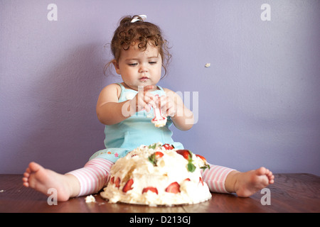 Cute baby girl playing with a birthday cake and number one candle. Stock Photo