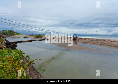 Suspension bridge over small river leading to the sea in Bali. Stock Photo