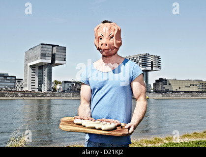 Germany, Cologne, Young man with pig mask holding sausage Stock Photo