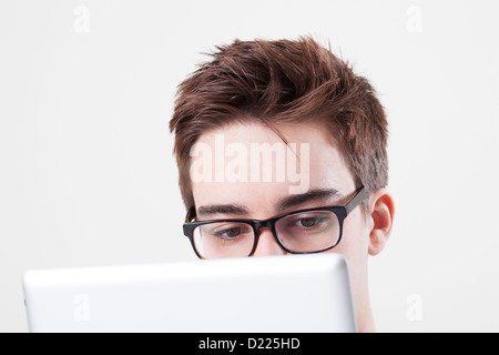 Young male wearing glasses looking at the screen of his laptop or digital tablet. Close up on eyes.