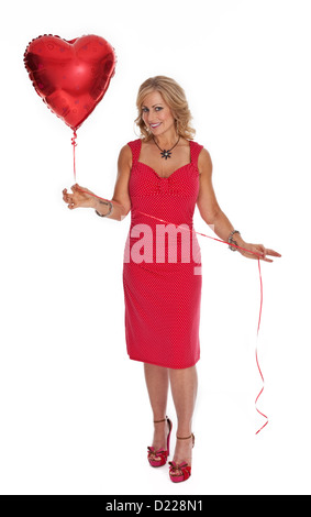 Full length photo of 40 year old woman in red dress holding heart shaped red balloon on white background. Stock Photo