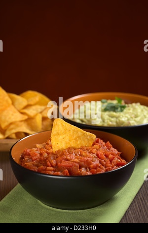 Tomato salsa with a nacho in it and guacamole sauce in the back (Selective Focus, Focus on the nacho in the tomato salsa) Stock Photo