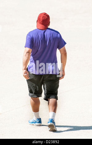 Man in shorts and turned reverse red cap walking away, rear view back / from behind Stock Photo