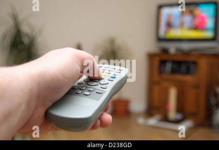 A hand holding a television remote control pointing at the television set. Stock Photo