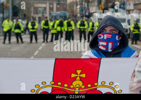 Belfast, UK. 12th Jan, 2013.  A Loyalist protester stands behind a Loyalist flag whilst a line of police stand in the background. The protesters are calling for the Union Flag to be raised on City Hall permanently. Later rioting broke in the Belfast Borough of Castlereagh. later rioting broke in the Belfast Borough of Castlereagh. Stock Photo