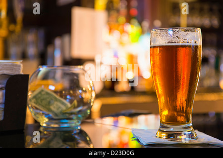 Fresh draft amber beer on a counter of a hotel bar, tip jar in the background Stock Photo