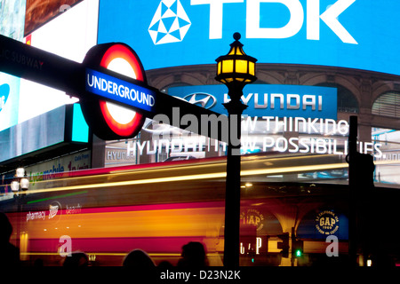 London Underground roundel at night with advertising LED screens behind Piccadilly Circus West End London England UK Stock Photo