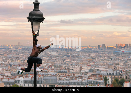 acrobatic performance artist at an old gas lamp on the hill of Sacre Coeur and view of Montmartre and Paris Stock Photo