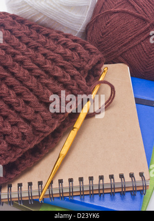 Brown crochet hat with golden hook, yarns and books. Stock Photo