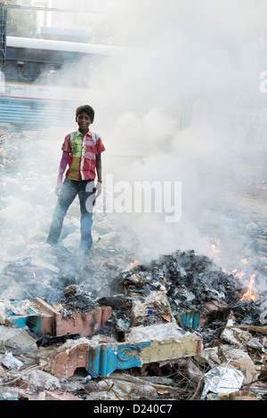Indian boy standing in amongst burning household waste. Andhra Pradesh, India