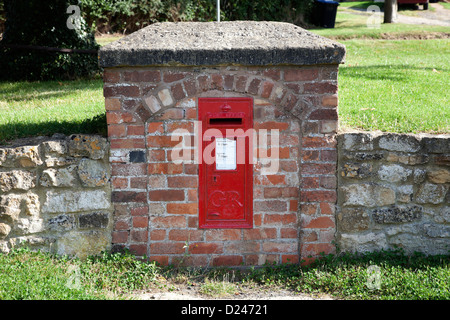 Red post box set into wall on village green Stock Photo