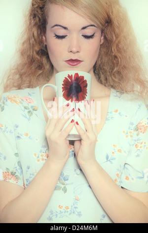 a woman in a floral dress is drinking out of a mug Stock Photo