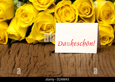 Yellow roses on old wooden board and a card with the german word "Dankeschön" Stock Photo