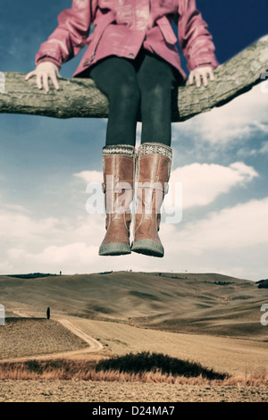 a girl sitting on a branch high over a field Stock Photo