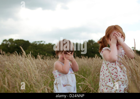 Two little girls playing hide and seek in a field Stock Photo