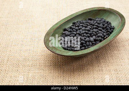 black turtle beans in a rustic wood bowl against burlap canvas Stock Photo