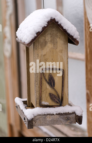 A hanging wooden birdfeeder sits empty beneath a mantle of winter snow. Stock Photo