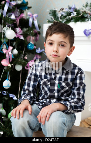 thoughtful boy in a plaid shirt sitting around the Christmas tree Stock Photo