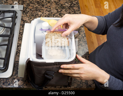 Female hands packing lunch into portable bag while in the kitchen on stone counter top next to stove Stock Photo