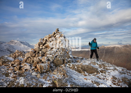 Walker on the Summit of Pike of Blisco in Winter with the Mountain of Bow Fell to the Left of the Cairn Lake District Cumbria UK Stock Photo