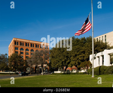 Flag at half mast flies in Dealey Plaza and The Sixth Floor museum  across Elm St where Lee Harvey Oswald shot Kennedy in 1963 Stock Photo