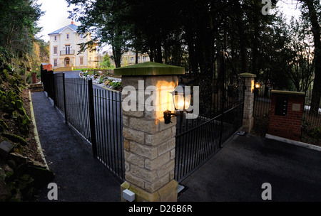 Large three storey newly built house in a woodland setting with a long drive and ornate wrought iron gates. Stock Photo