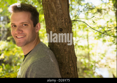 USA, Connecticut, Newtown, Portrait of young man leaning against tree trunk Stock Photo