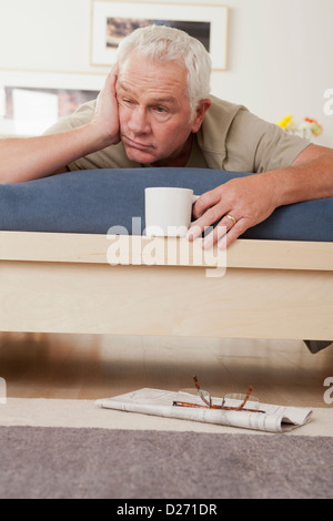 Tired senior man holding coffee cup lying on bed Stock Photo
