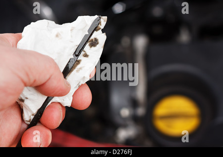 Checking the engine oil level on a car dipstick during its regular service, oil cap and engine in background Stock Photo