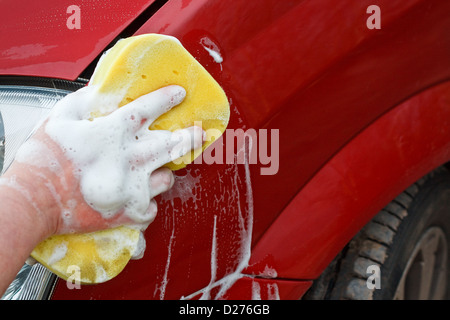 Washing the front wing of a car by hand with a yellow soapy sponge Stock Photo