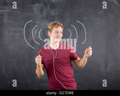 Studio shot of mid adult man listening to music on earphones and dancing with chalk drawing on blackboard Stock Photo