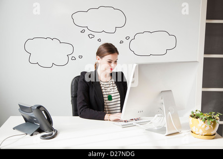 Studio shot of young woman working at desk with thought bubbles around her head Stock Photo