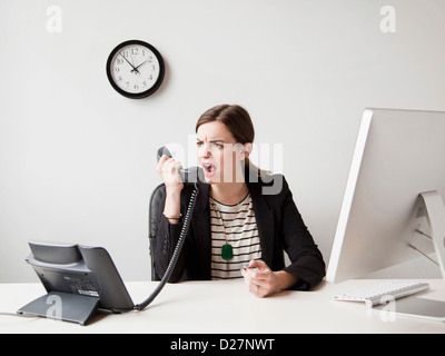 Studio shot of young woman working in office yelling into phone Stock Photo