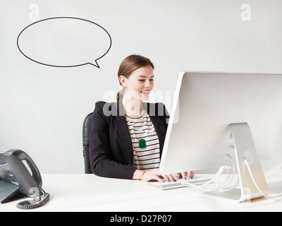 Studio shot of young woman working on computer with speech bubble next to her head Stock Photo