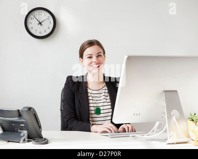 Studio shot portrait of young woman working on computer and smiling Stock Photo