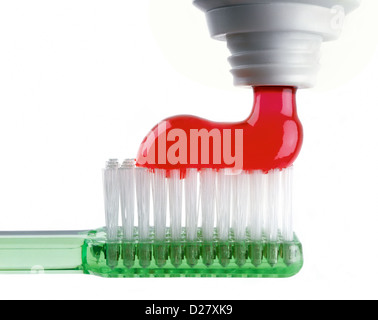 Red Toothpaste Being Squeezed out onto Green Translucent Toothbrush on White Background Stock Photo