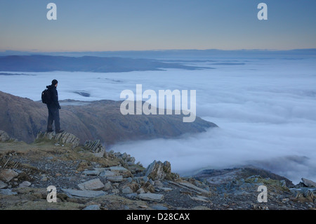 Walker above a temperature inversion on the summit of the Old Man of Coniston at dusk in the English Lake District Stock Photo