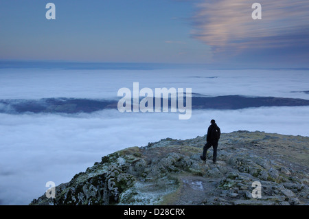 Walker on the summit of the Old Man of Coniston above a sea of cloud in the English lake District Stock Photo